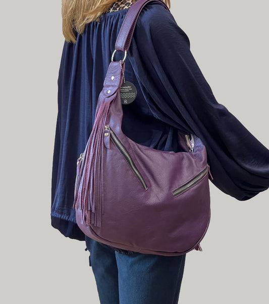 Person wearing a purple handbag with double fringe details on a plain background