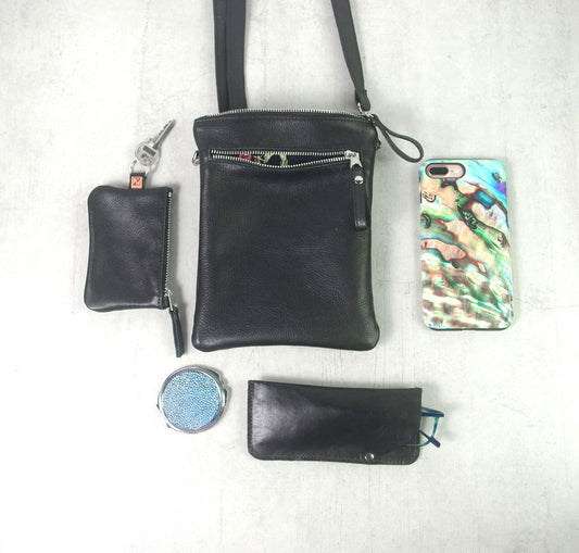 Black handbag with smaller black pouches, a phone case, and a compact mirror on a white background