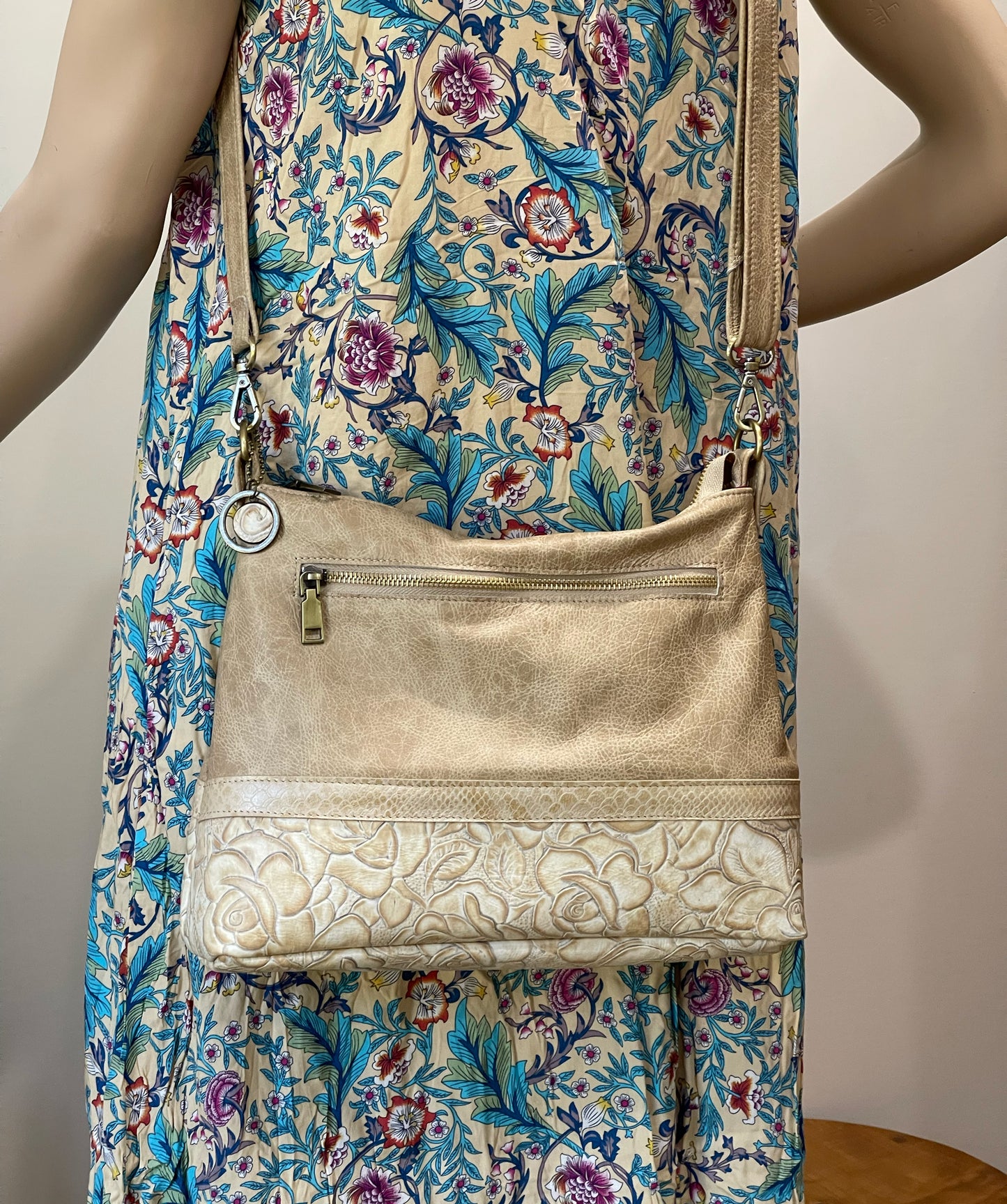 beige handbag with floral patterned leathers on bottom half, with leather metal charm worn on matching floral dress