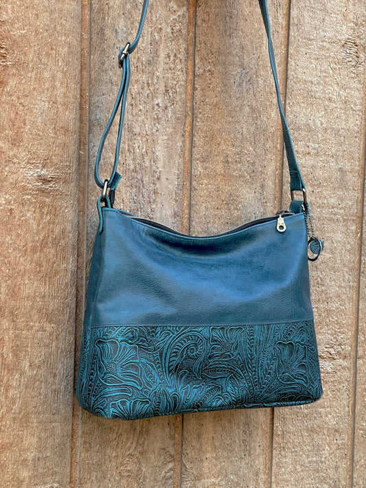 Teal Blue leather handbag with floral embossing on a wooden surface