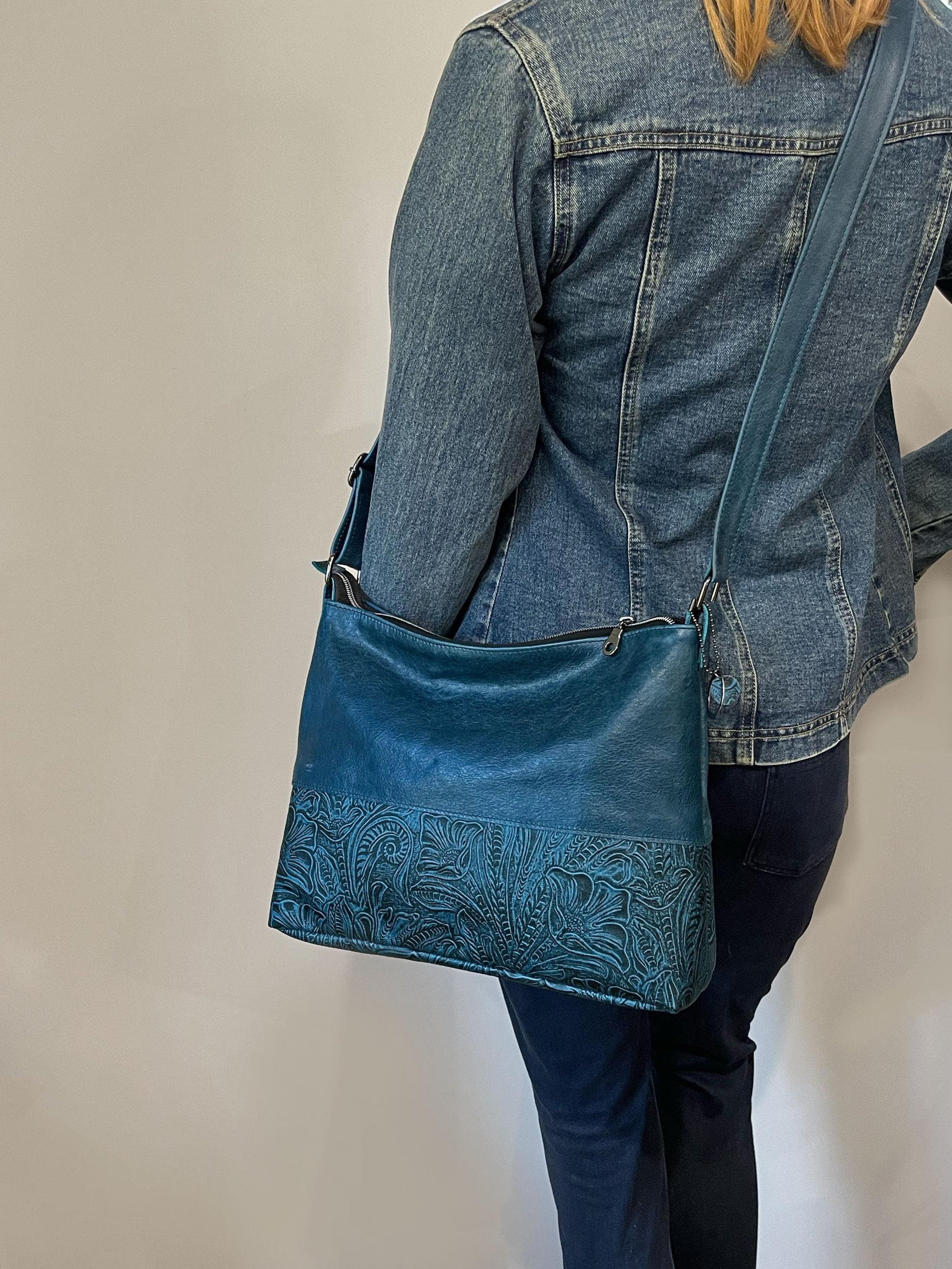 Person wearing a blue denim jacket and carrying a matching Teal blue handbag with tooled garden design.