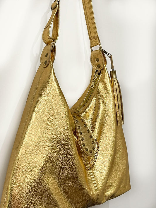 Gold leather handbag with studded detail on a white background. top gold zipper