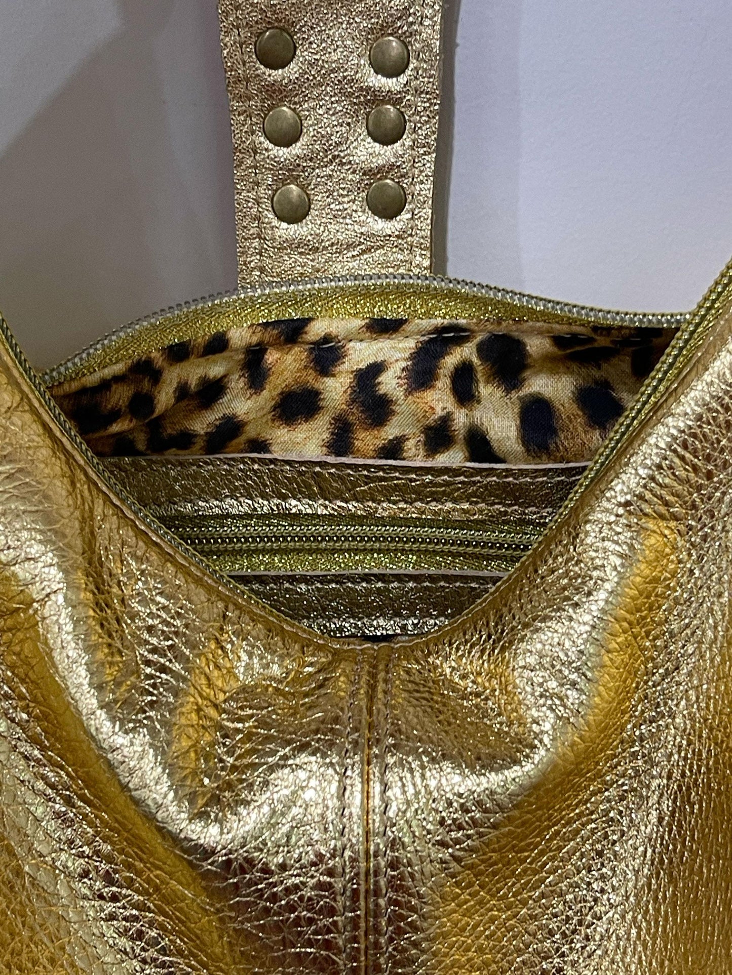metallic Gold handbag with leopard print interior on a light gray background. inside zipper pocket