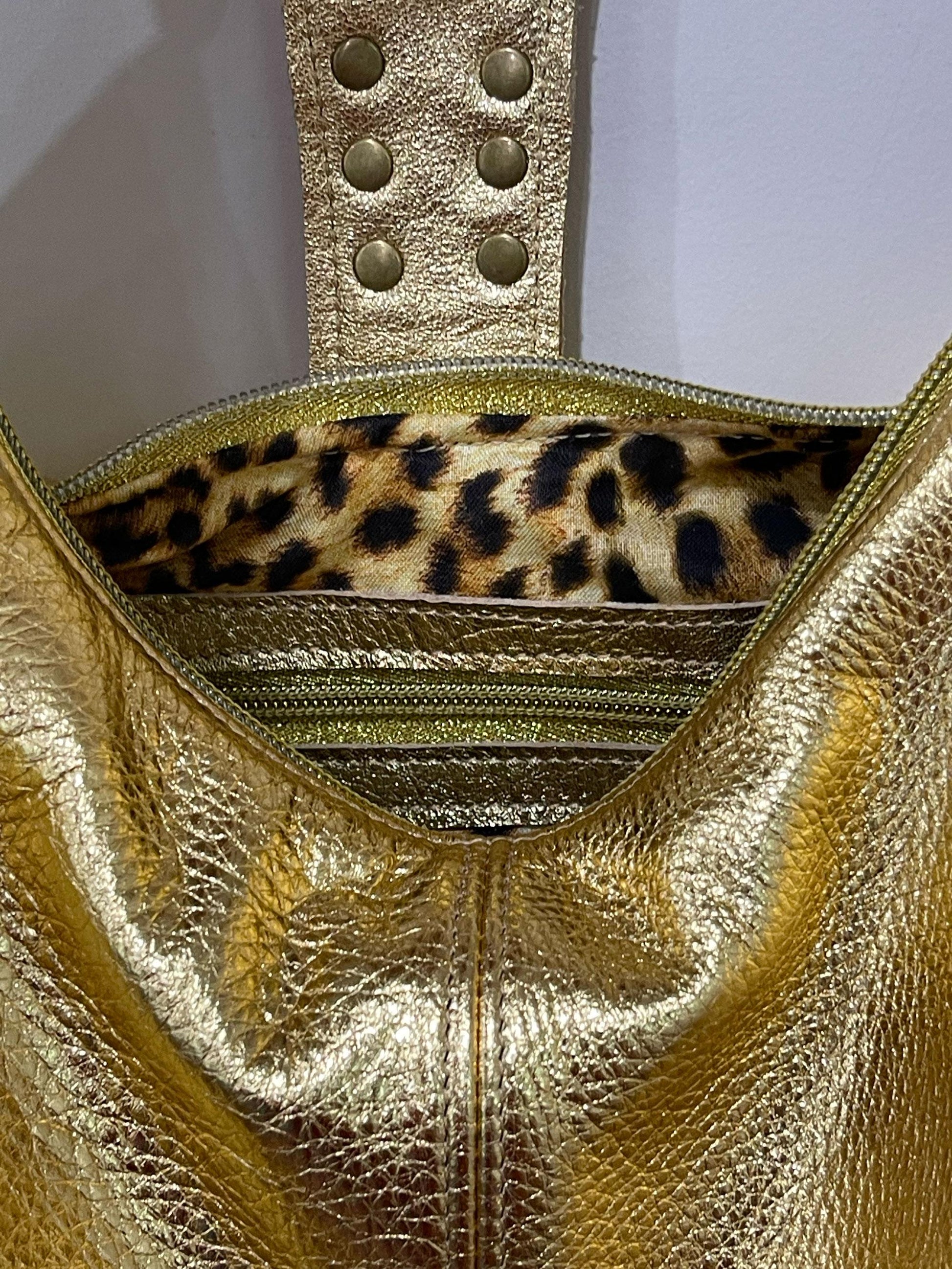 metallic Gold handbag with leopard print interior on a light gray background. inside zipper pocket