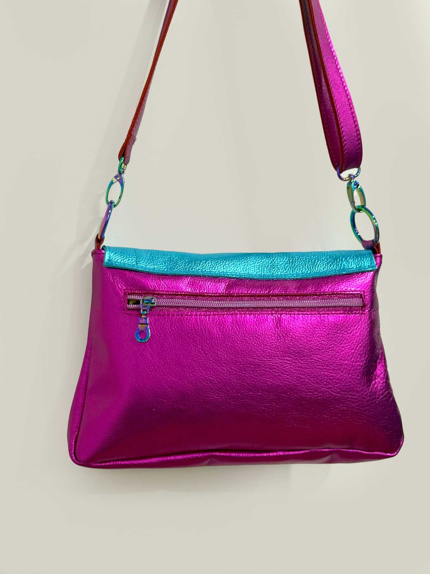 fuchsia pink metallic leather handbag showing reverse side with pink iridescent zipper pocket and rainbow zipper pull. detachable adjustable length strap
