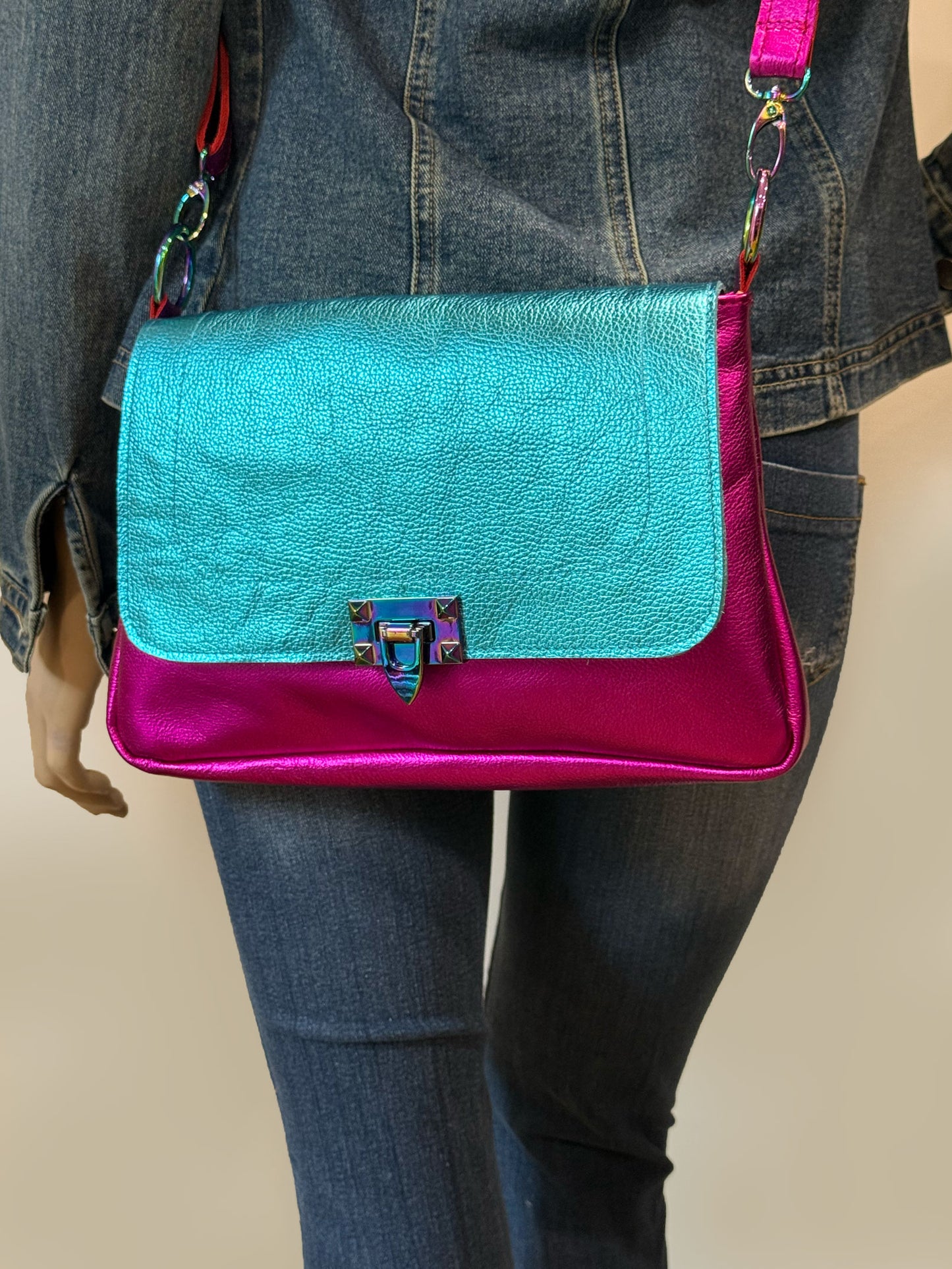 close up of pebble leather turquoise and pink handbag, with rainbow metal clasp closure on flap with a person wearing jeans