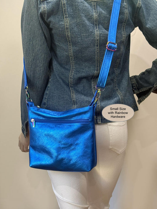 Person wearing a blue crossbody bag with rainbow hardware on a plain background