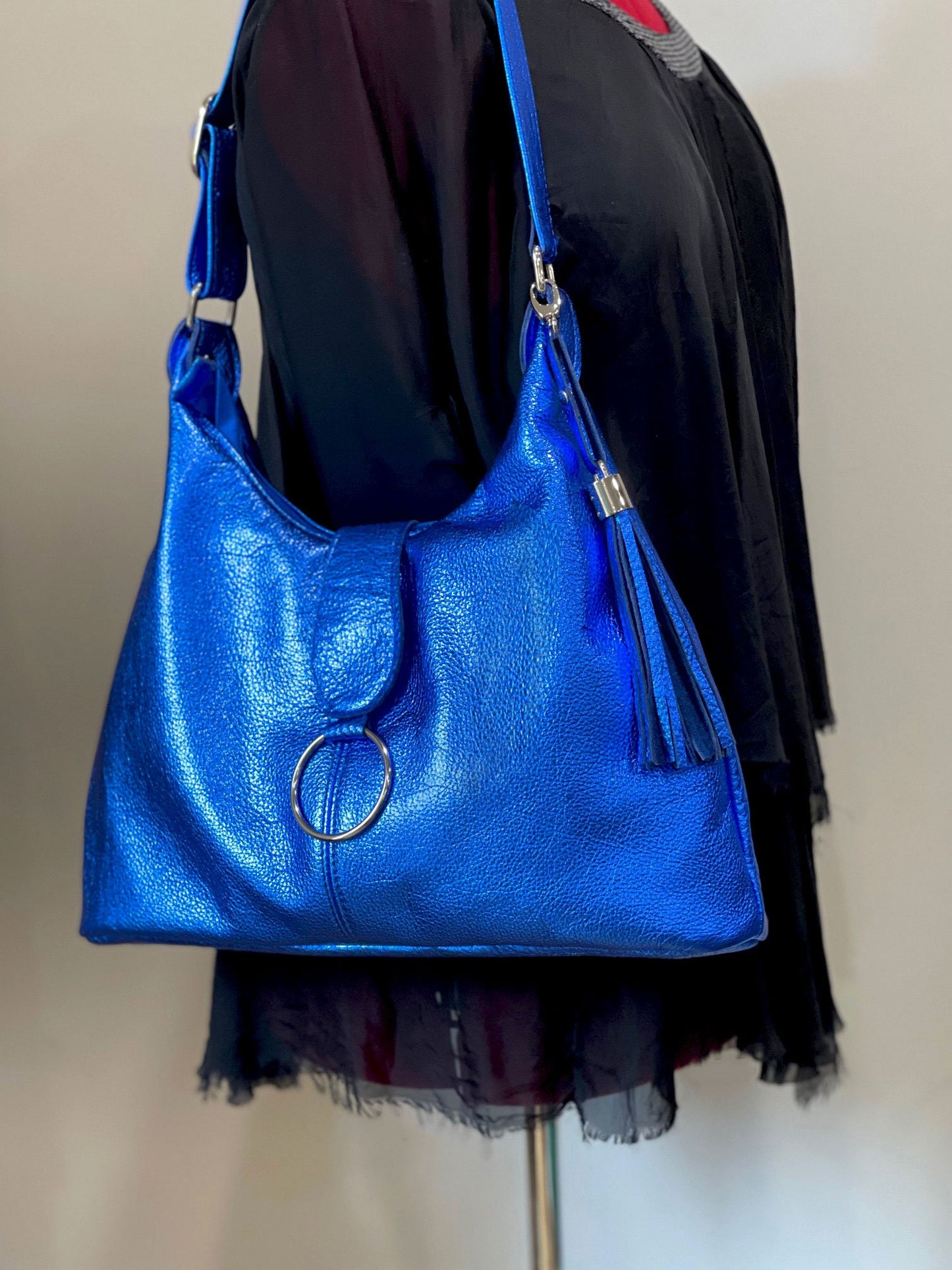bright blue metallic handbag with a circular clasp and a leather tassel silver hardware on a mannequin.