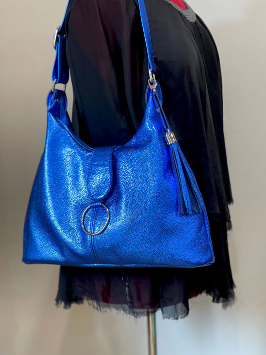bright blue metallic handbag with a circular clasp and a leather tassel silver hardware on a mannequin.