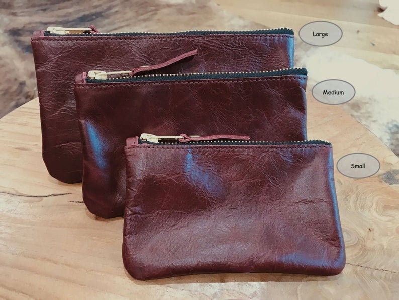 Three burgundy leather pouches of different sizes on a wooden surface