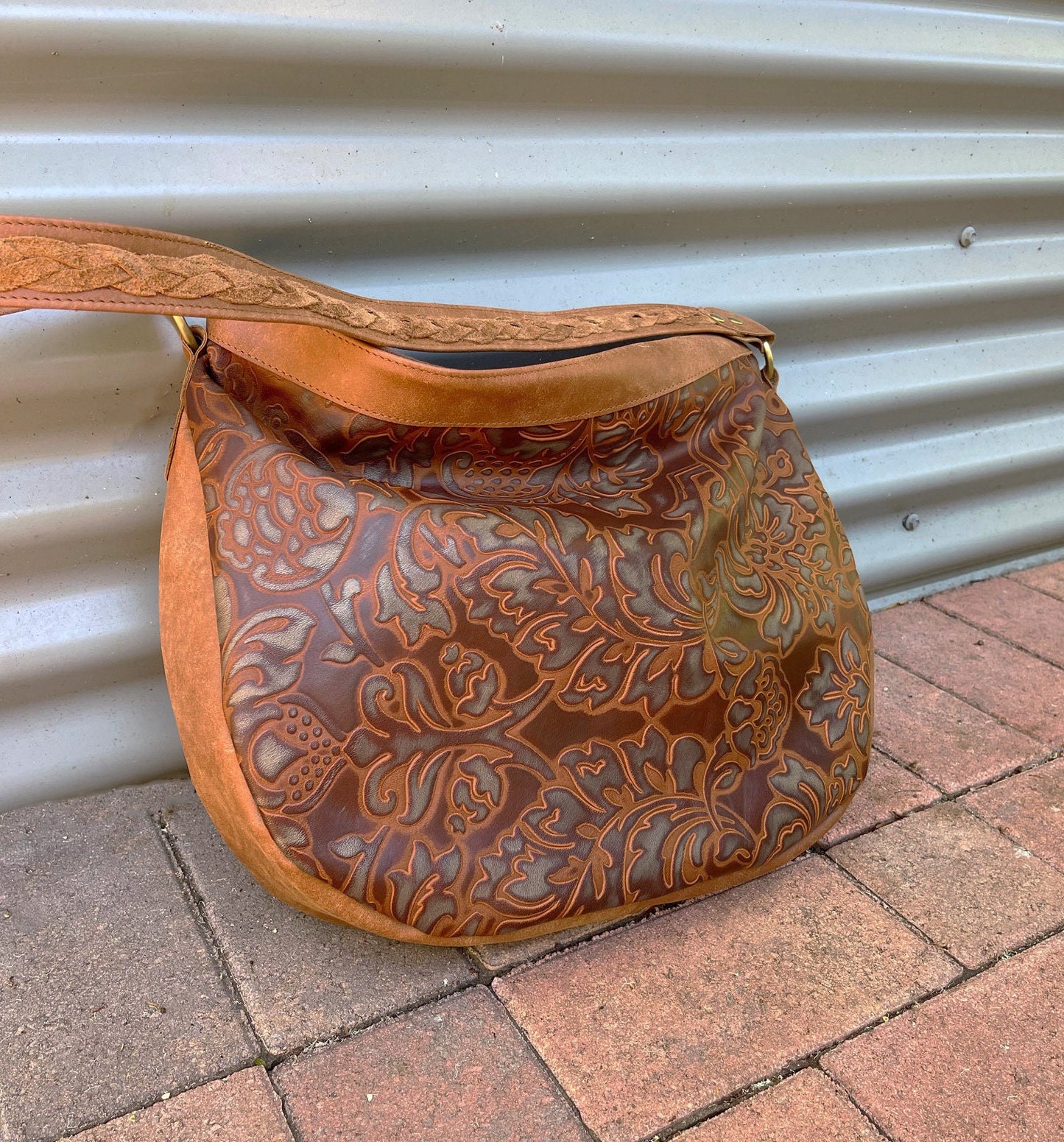 tooled brown leather handbag with abstract leaf patterns and a woven feature on the strap.