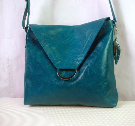 Teal leather handbag with a silver clasp on a white surface. flap with magnet closure