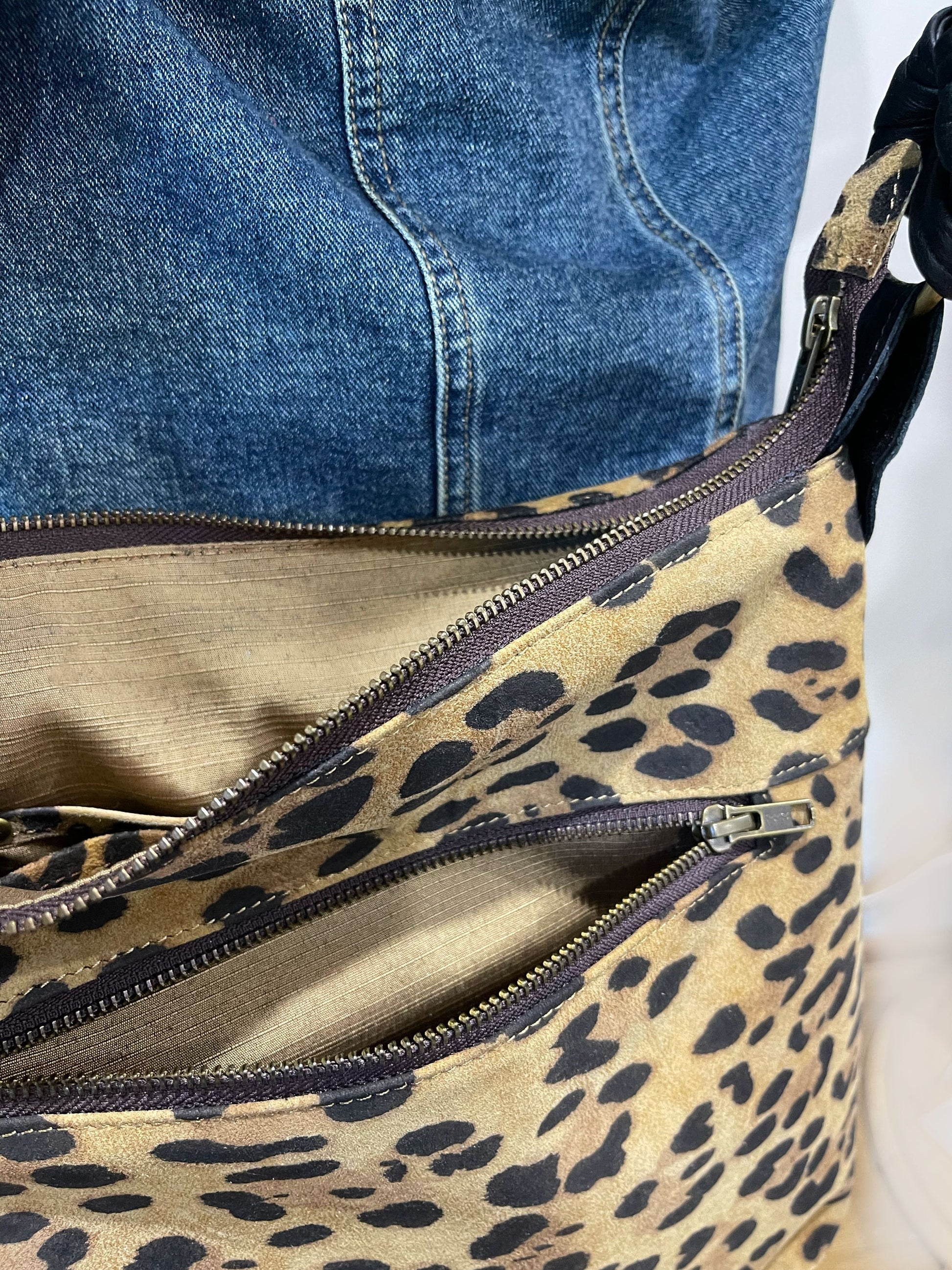 close up of Leopard print bag with zipper closure bronze hardware against a denim jacket.