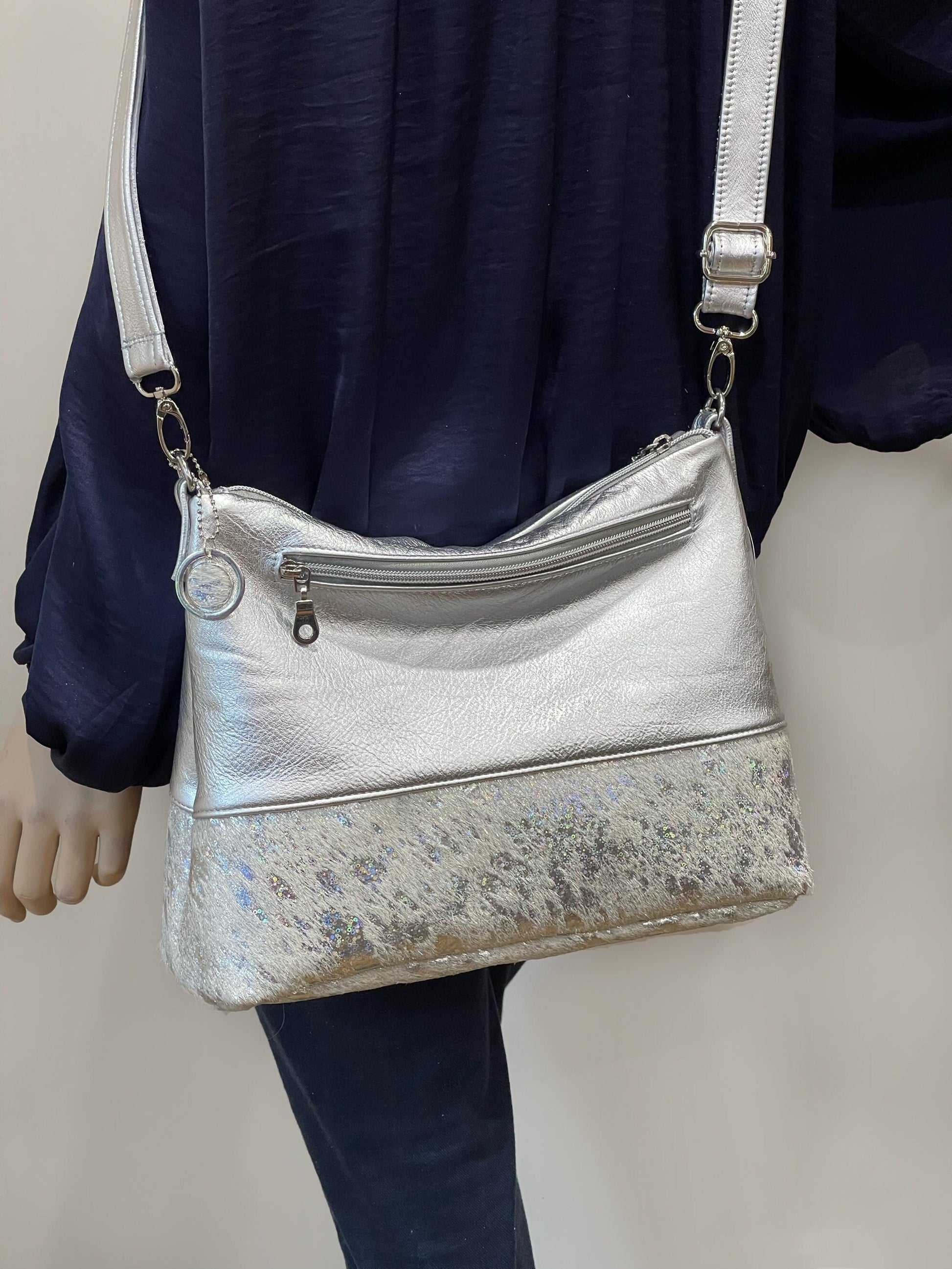 Silver handbag with a white holographic cowhide bottom section worn by a person against a neutral background