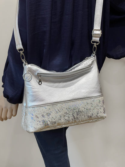 Silver handbag with a white holographic cowhide bottom section worn by a person against a neutral background