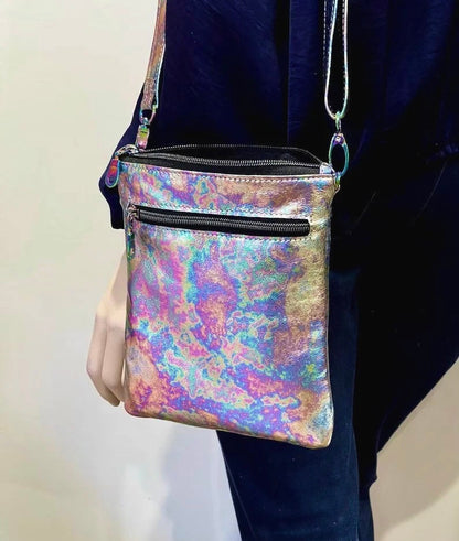 Multi colour Oil Spill crossbody bag held by a person against a neutral background. top zipper closure