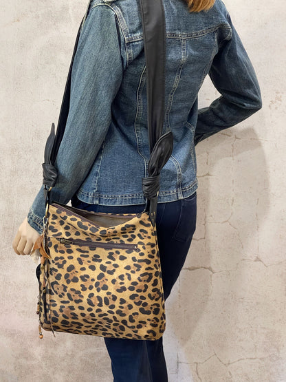 Person wearing a leopard print bag over their shoulder with outside zipper pocket and black strap and top zipper closure.