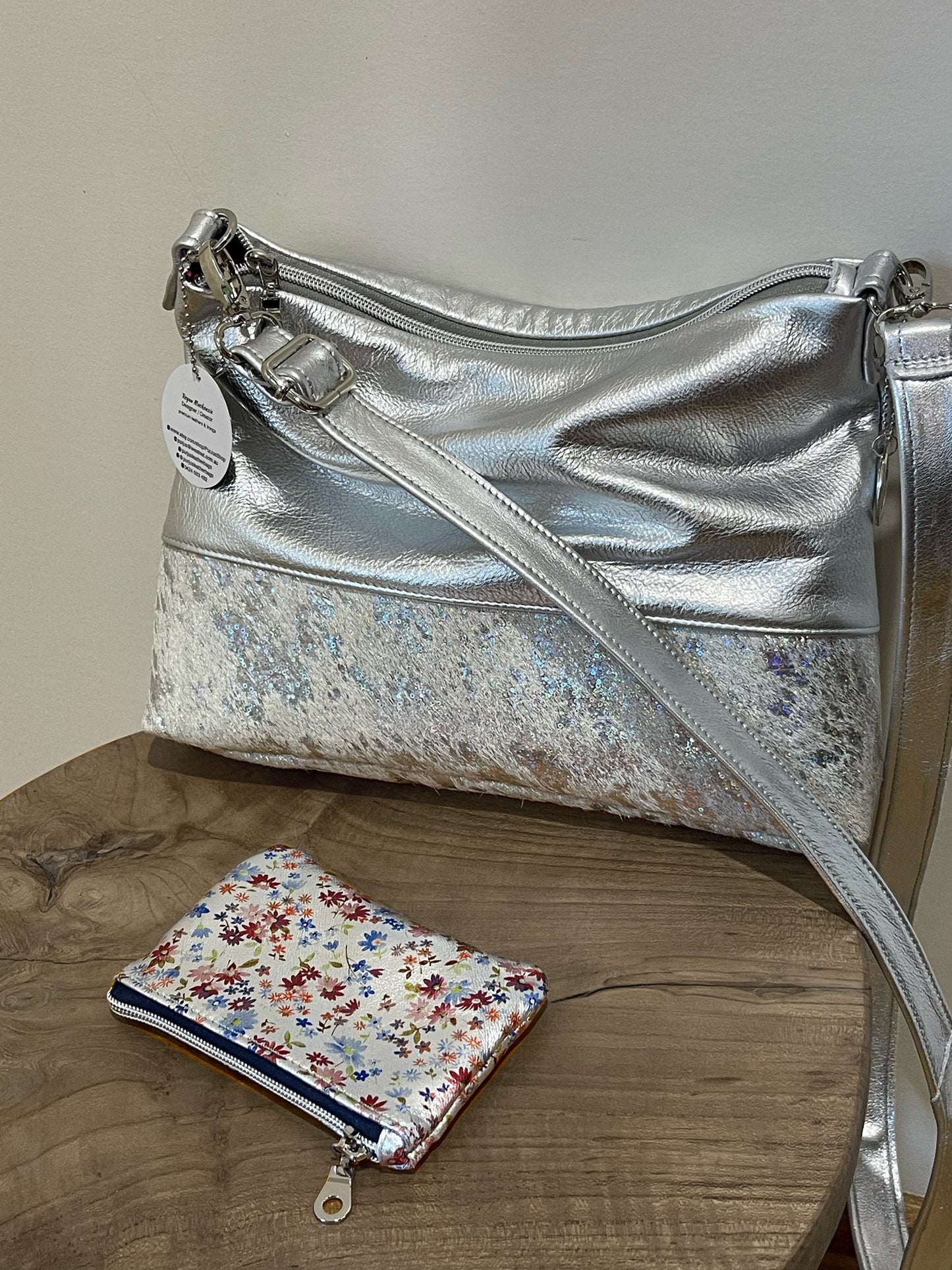 Silver metallic handbag with a floral pouch. adjustable leather strap and top zipper closure. silver hardware