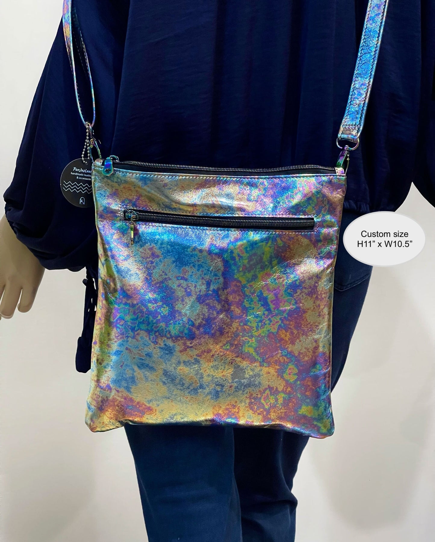 Multicolored iridescent crossbody bag held by a person wearing a dark blue outfit.