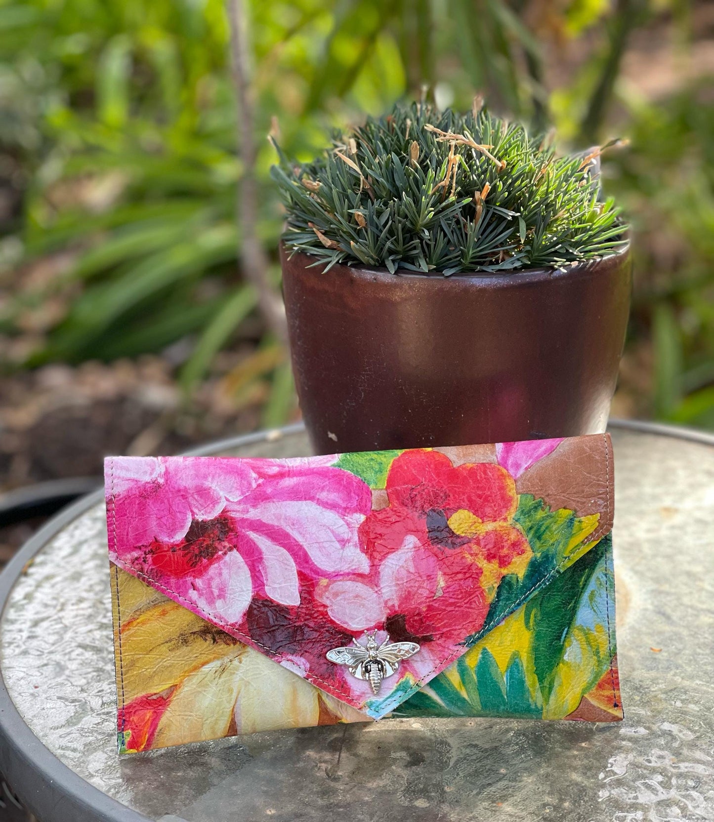 Colorful abstract floral wallet with a silver moth clasp on a glass surface with a potted plant in the background