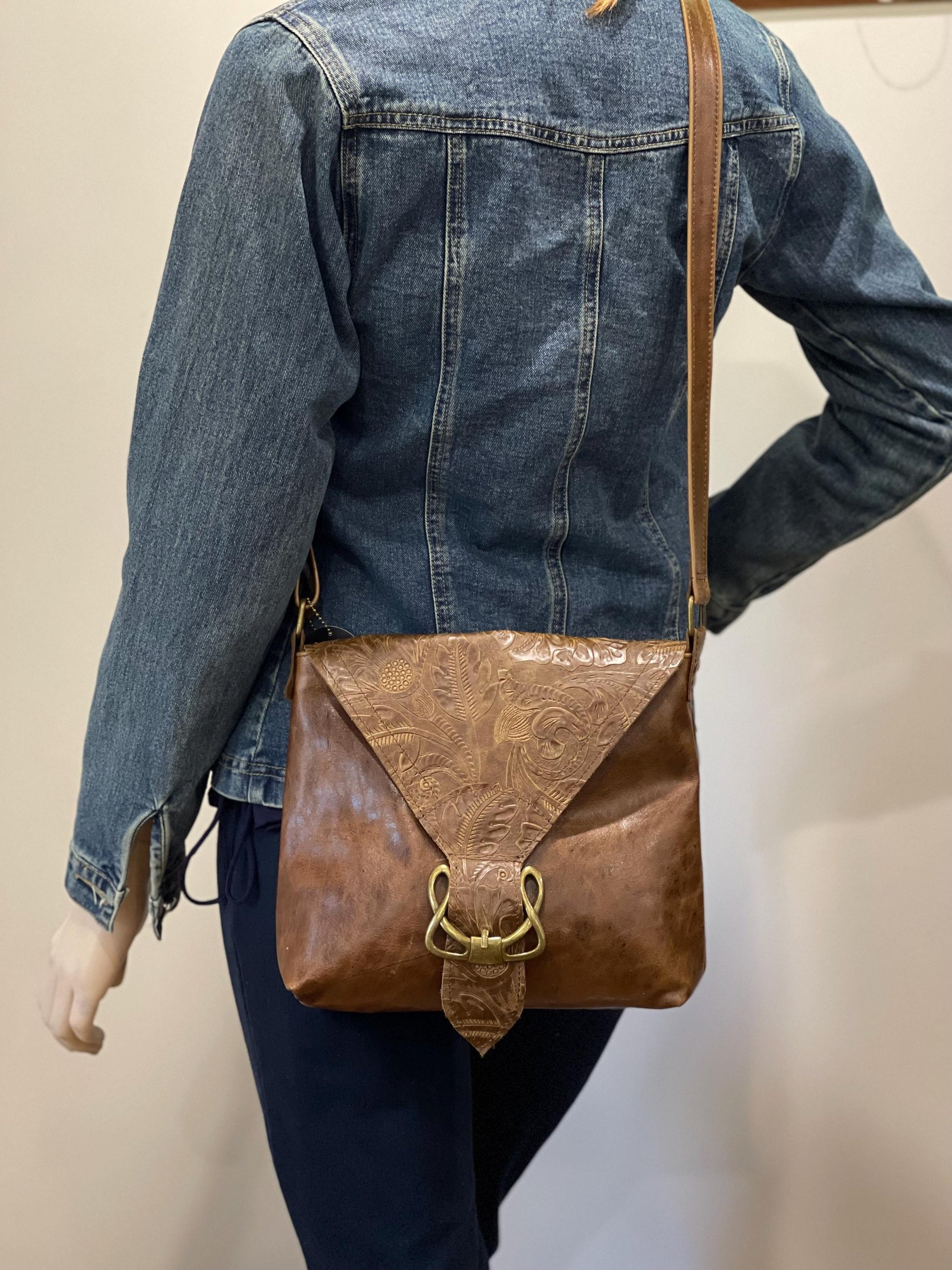 Person wearing a denim jacket with a brown leather bag over their shoulder against a plain background