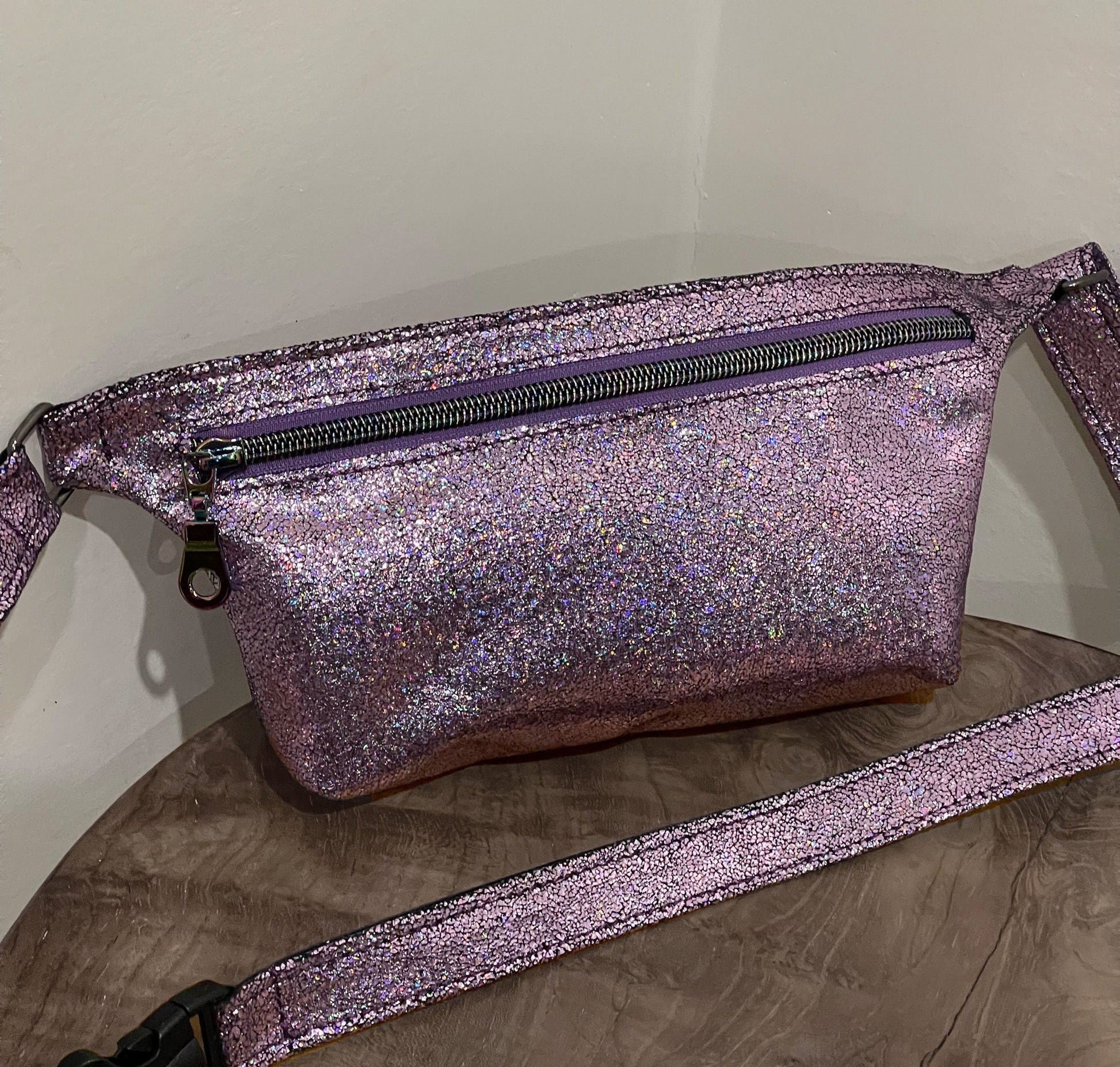 Pink glittery fanny pack waist bag on a wooden surface with a neutral background