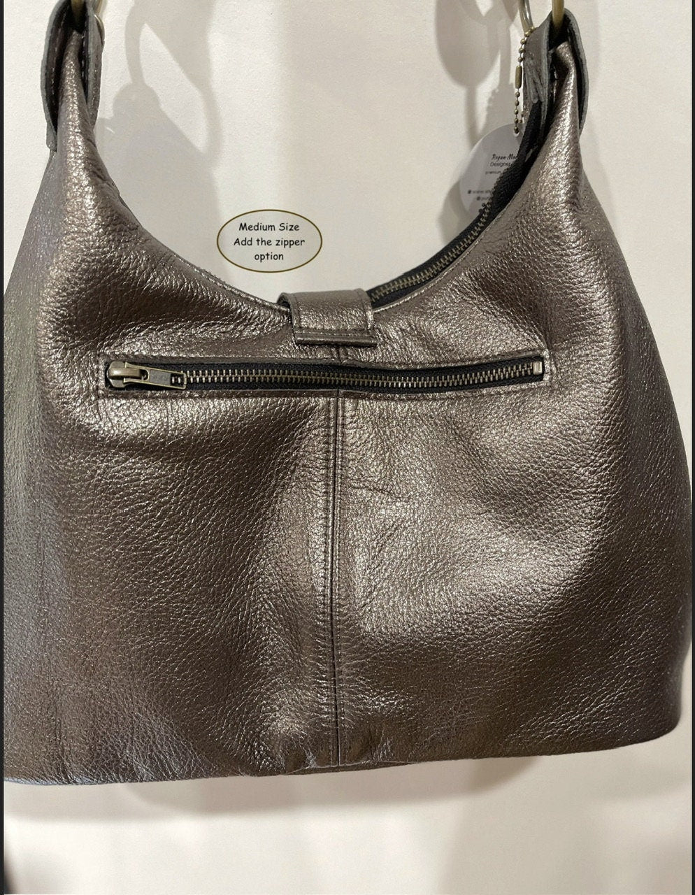Pewter leather handbag with bronze zipper pocket outside a visible brand label on a white background