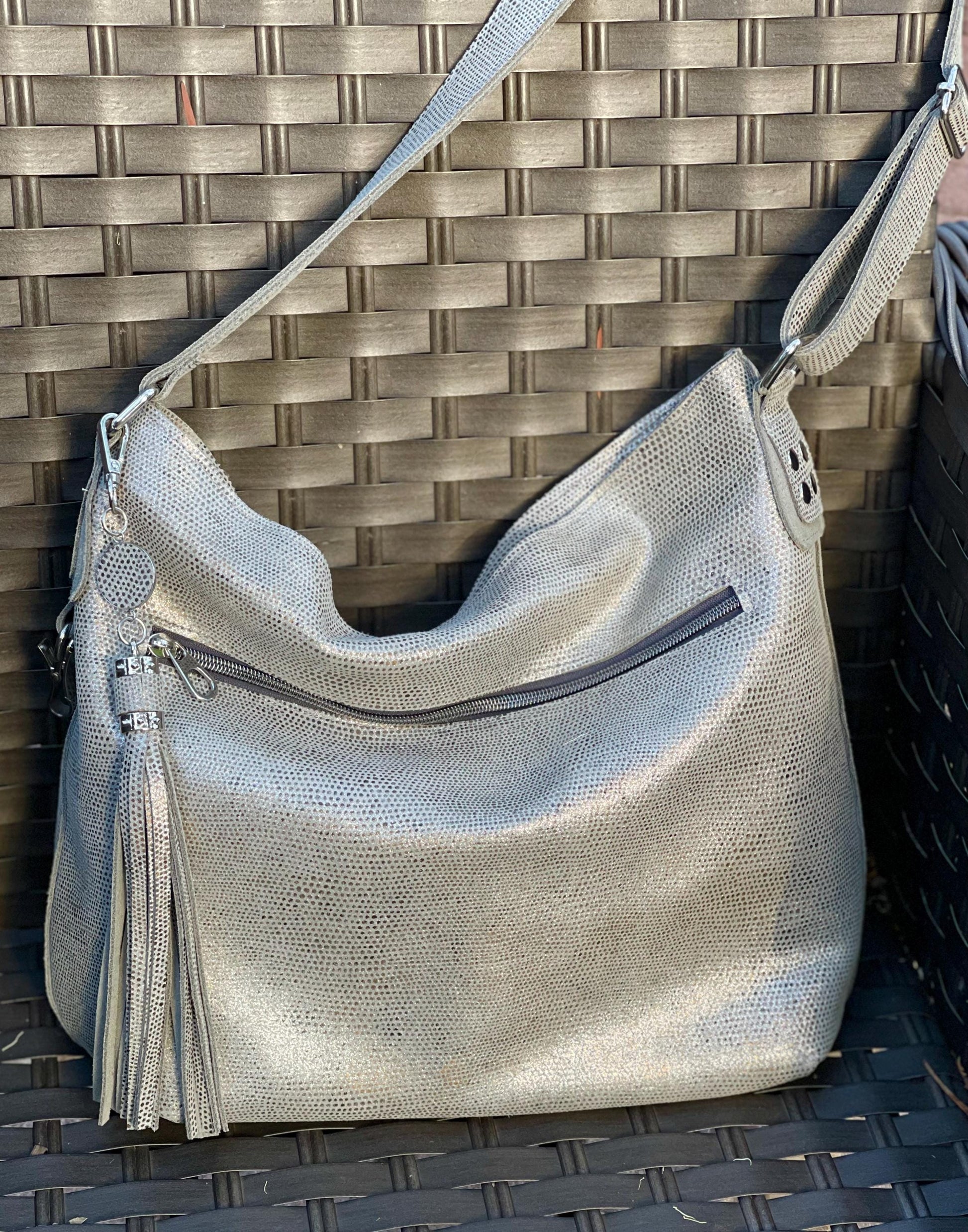 Silvery pearl leather handbag with wide zipper pocket and a lightly textured surface on a woven surface