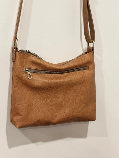 Brown leather handbag with embossed design on a beige background