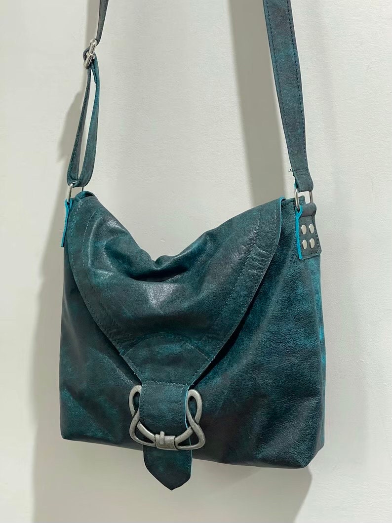 vintage Teal leather handbag with silver celtic buckle and flap closure on a white background