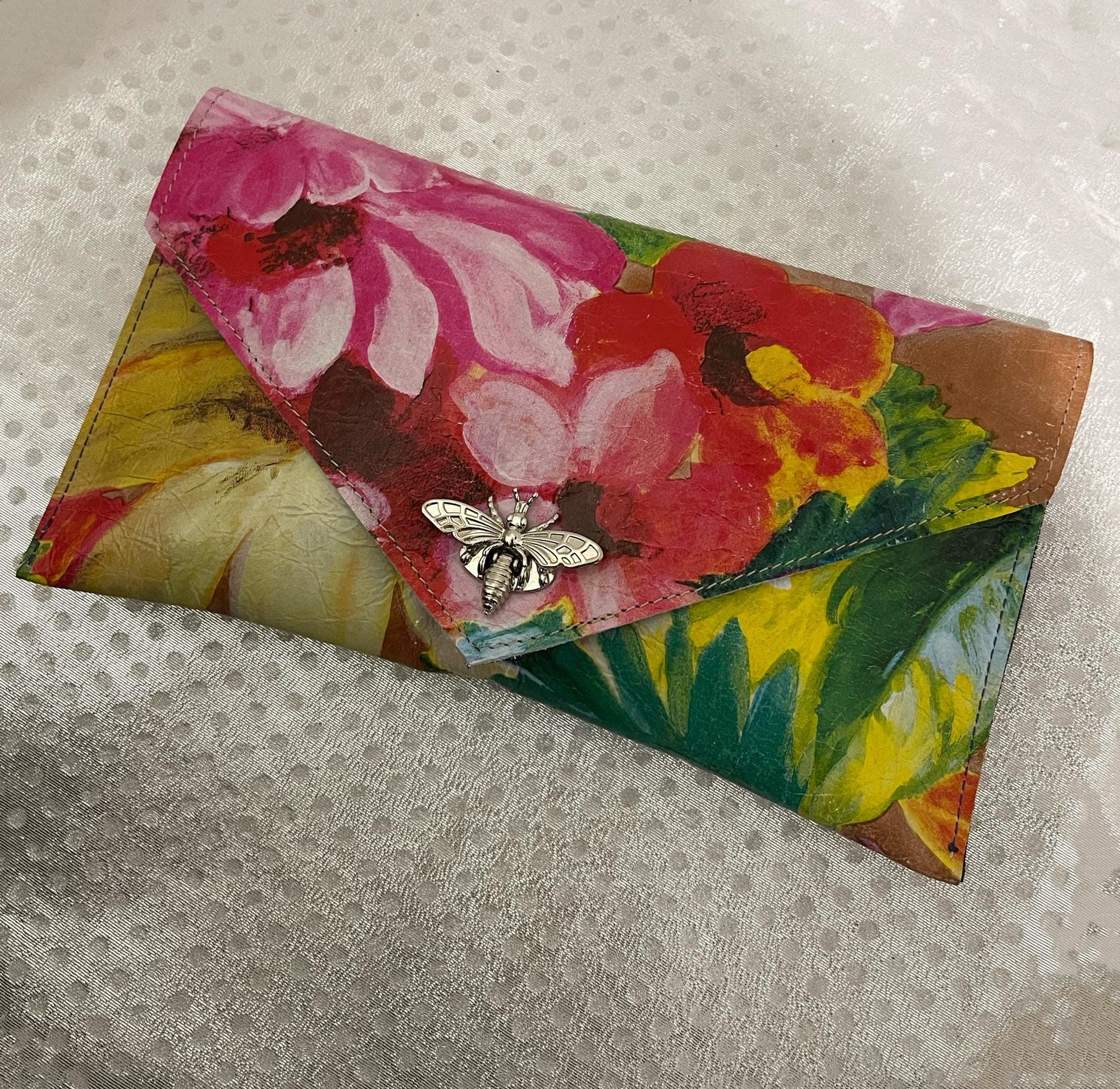 Floral-patterned clutch bag with a bee charm clasp closure on a textured surface
