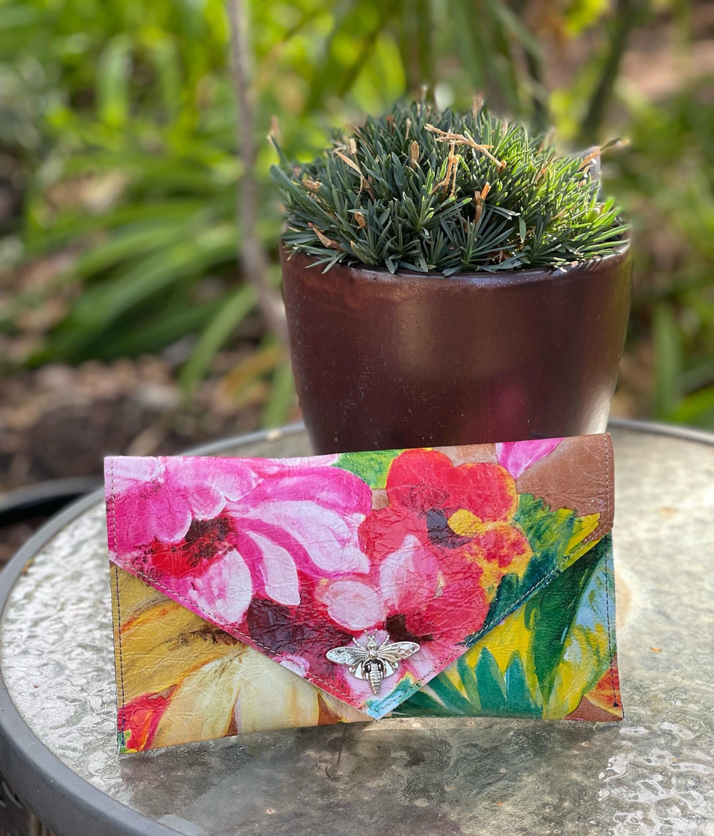 painted colorful Floral-patterned clutch with a metal bee clasp closure on a reflective surface 