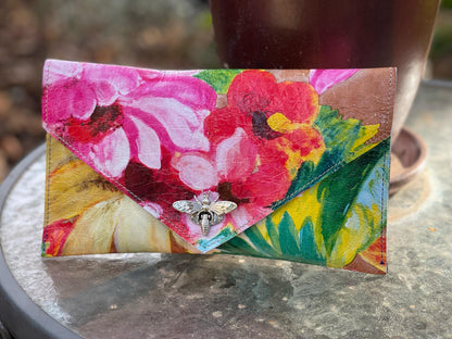 Floral patterned clutch bag with a bee charm on a reflective surface.