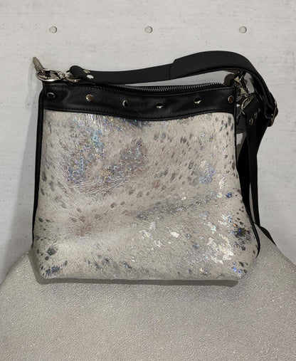 Silver glittery handbag with black strap on a light gray surface