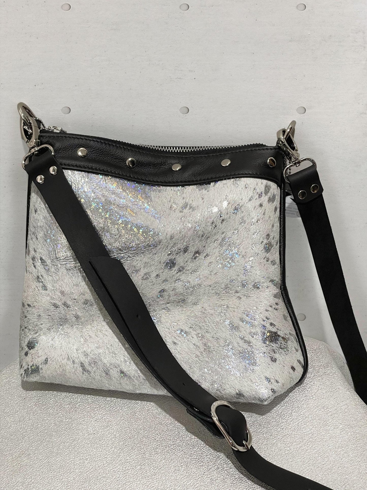 Silver glittery crossbody bag with black strap on a gray background