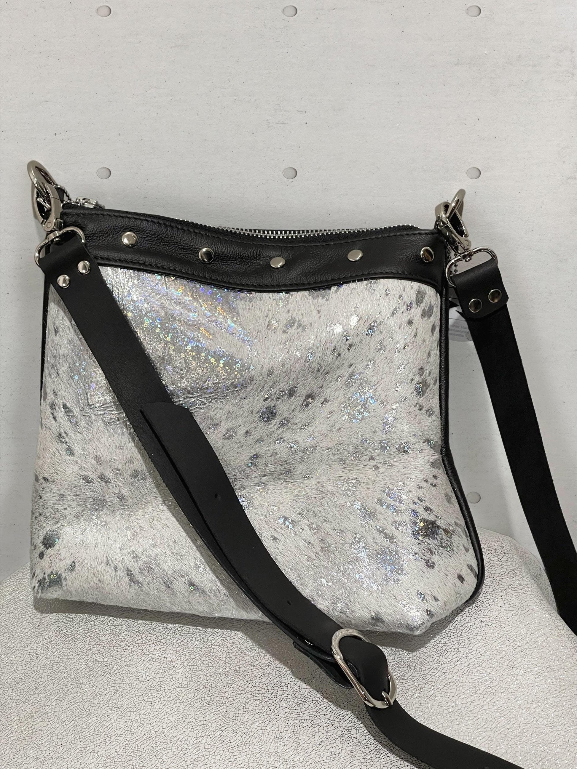 Silver glittery crossbody bag with black strap on a gray background