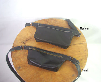 Two black waist bags, one medium and one small, on a wooden surface with a white background.