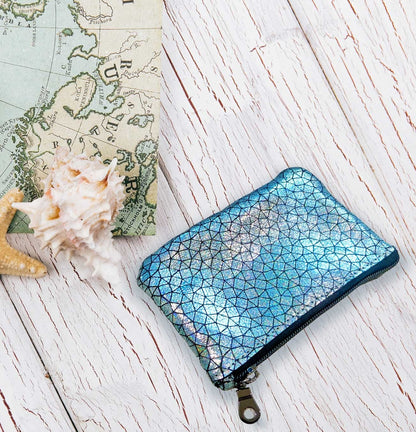 Blue geometric patterned holographic zipper pouch in a travel beach scene