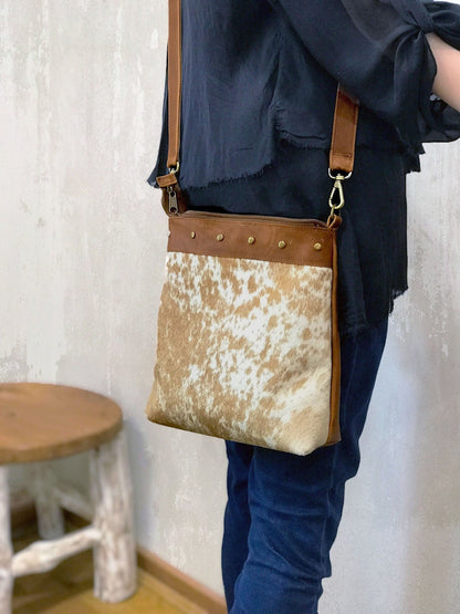 Person wearing a crossbody bag with cowhide hair leather design and brown leather accents.