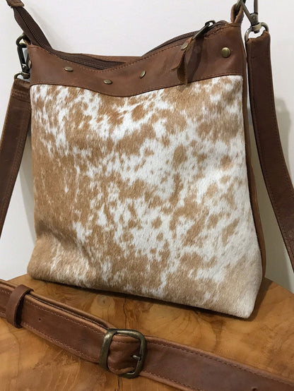 close up of tan and white cowhide leather bag on a wooden surface with a white background