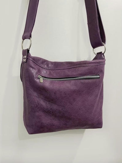 Purple leather shoulder bag with a visible zipper on a light gray background