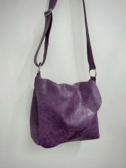 Purple leather handbag with asymmetrical flap and adjustable strap on a white background