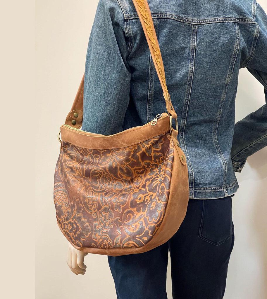 Person wearing a brown leather bag on shoulder with floral tooled patterns and tan leather sides