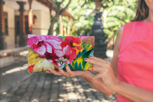 Woman holding a colorful floral clutch with silver metal bee clasp closure, in an outdoor summery setting. great for a wedding or lunch out with friends