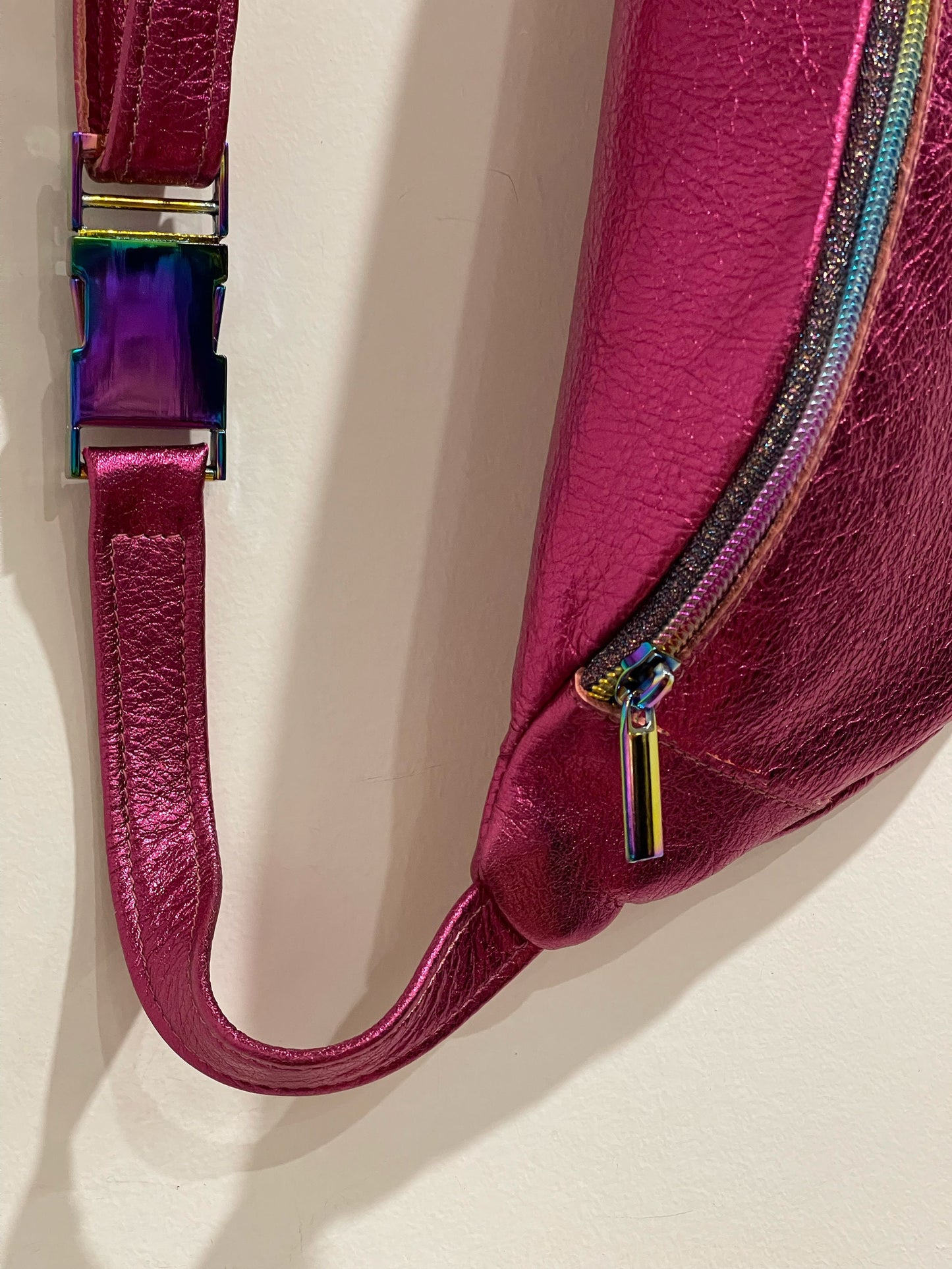 Close-up of metallic pink leather fanny pack with a colorful zipper pull on a light background