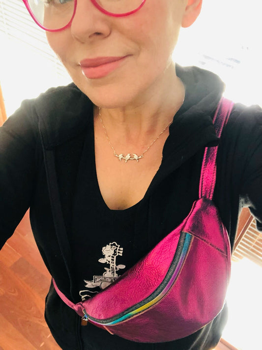 Person wearing a black top holding a metallic pink leather waist bag and wearing it as crossbody multipurpose.