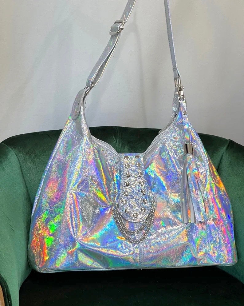 Holographic handbag with embellishments  chain and leather tassel sitting on a velvet chair