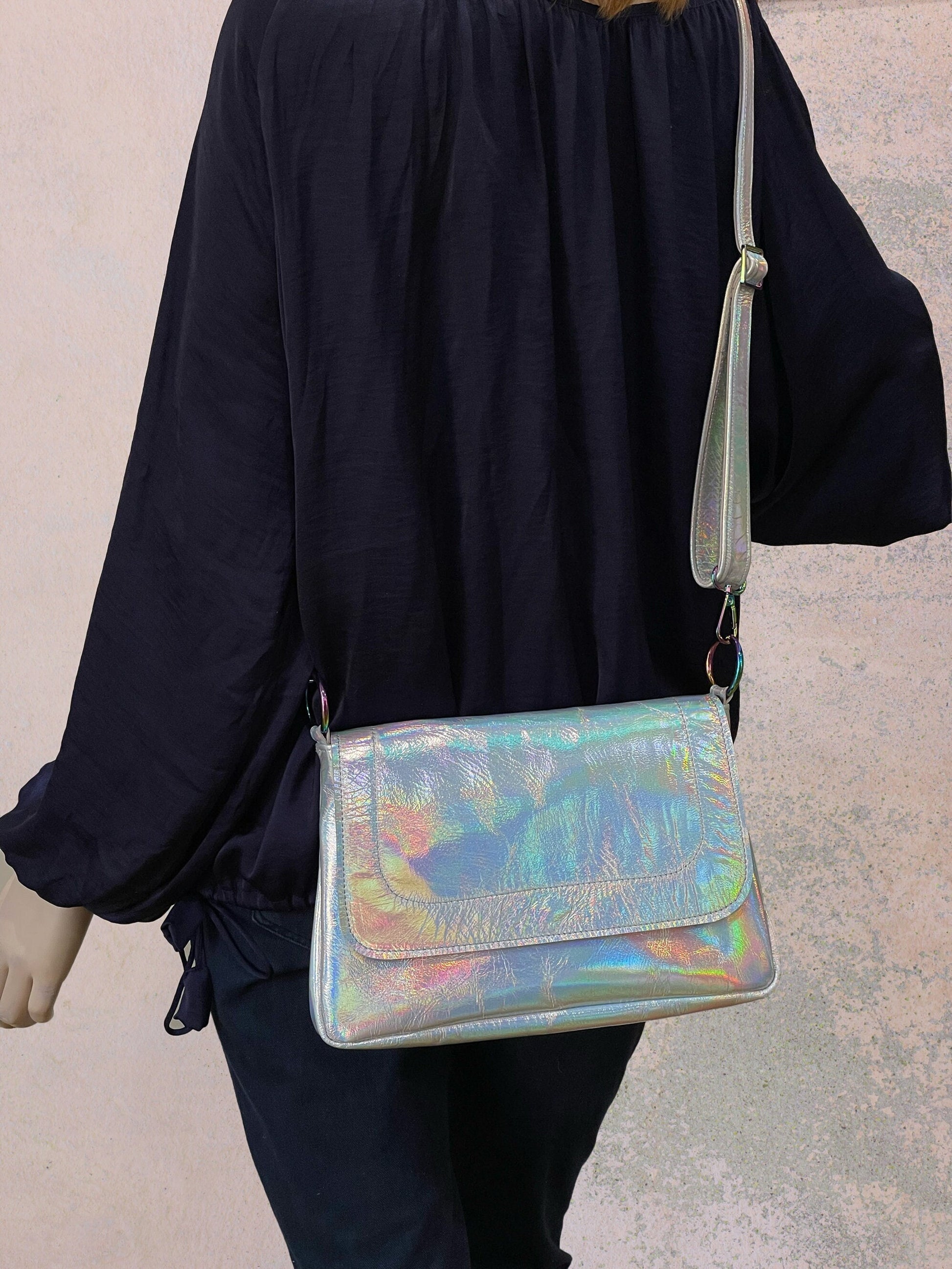 Person wearing a navy outfit with a holographic handbag across body with adjustable strap on a neutral background