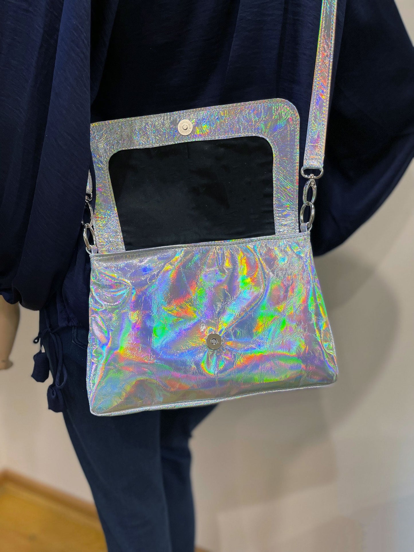Holographic crossbody with open lined flap showing magnet closure held by a person against a neutral background