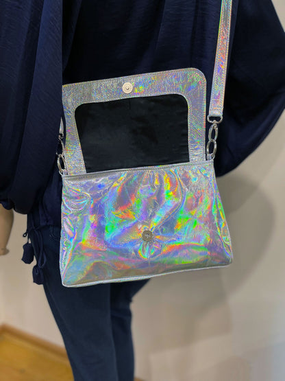 Holographic crossbody with open lined flap showing magnet closure held by a person against a neutral background